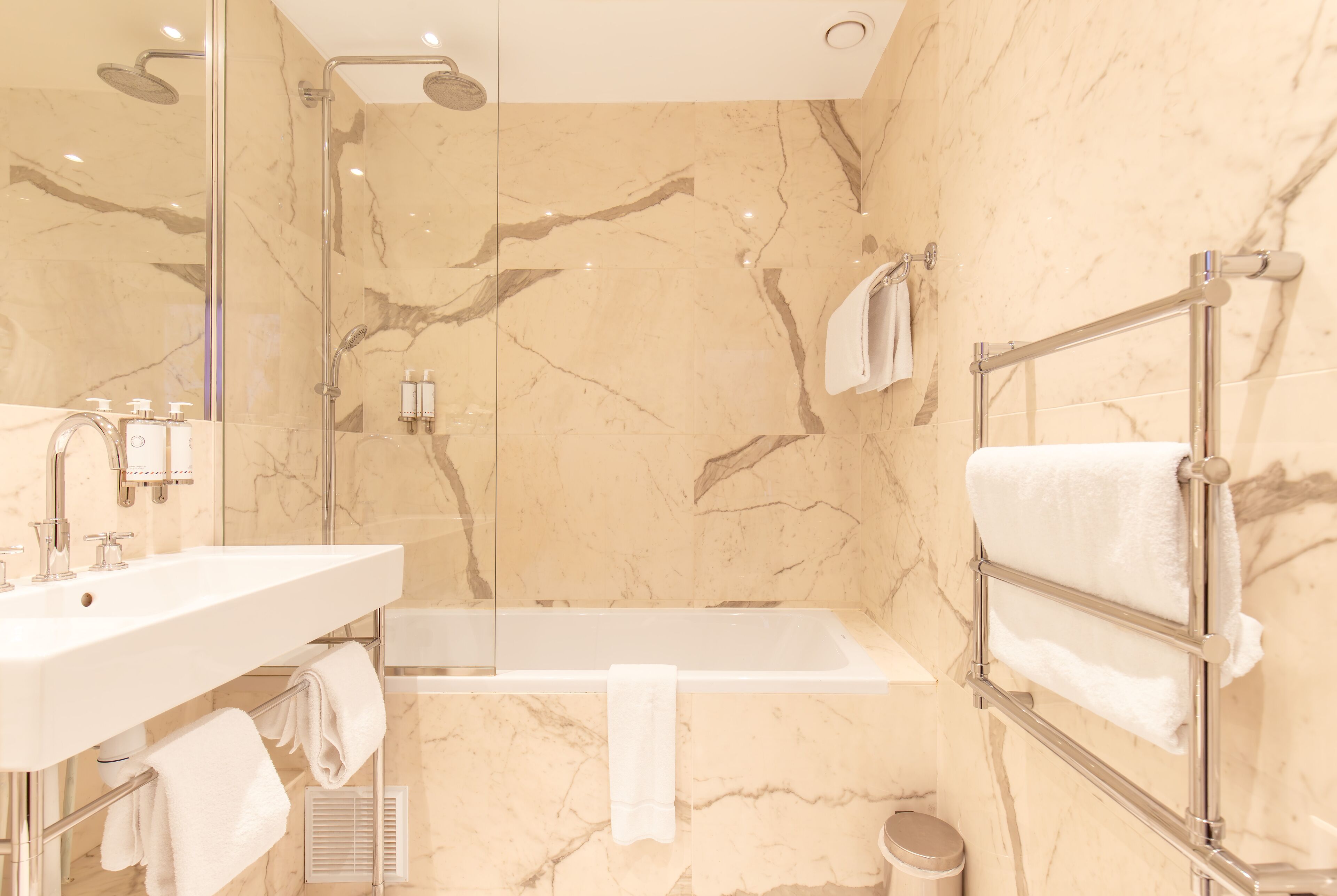 A modern bathroom with a marble wall, a bathtub, a glass-enclosed shower, and a towel rack with multiple towels.