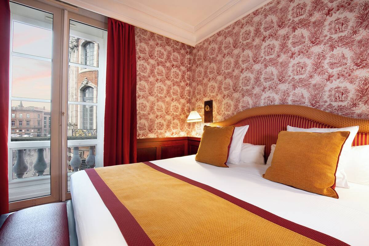 Habitación de hotel con una cama grande, vista panorámica de la ciudad a través de una ventana y un papel tapiz decorado.