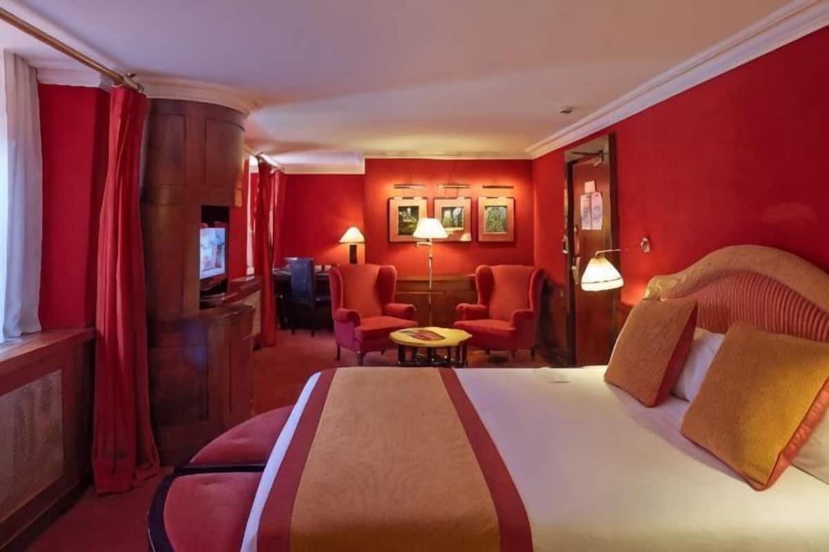 Habitación de hotel con una cama grande, dos sillones, una mesita y un escritorio con lámpara.