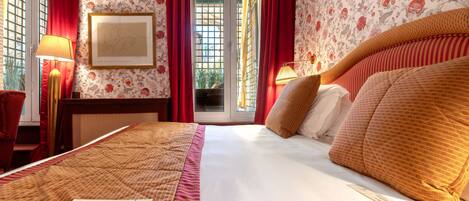 Una habitación de hotel con una cama grande, cortinas rojas, papel tapiz floral y un cuadro en la pared.