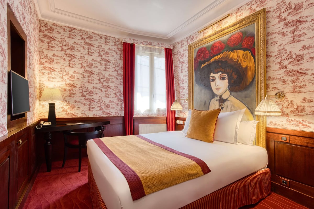 Una habitación de hotel con una cama grande, un escritorio, una silla, un televisor y un cuadro en la pared.