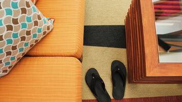 A room with a sofa, a patterned pillow, a striped rug, and a pair of black slippers.