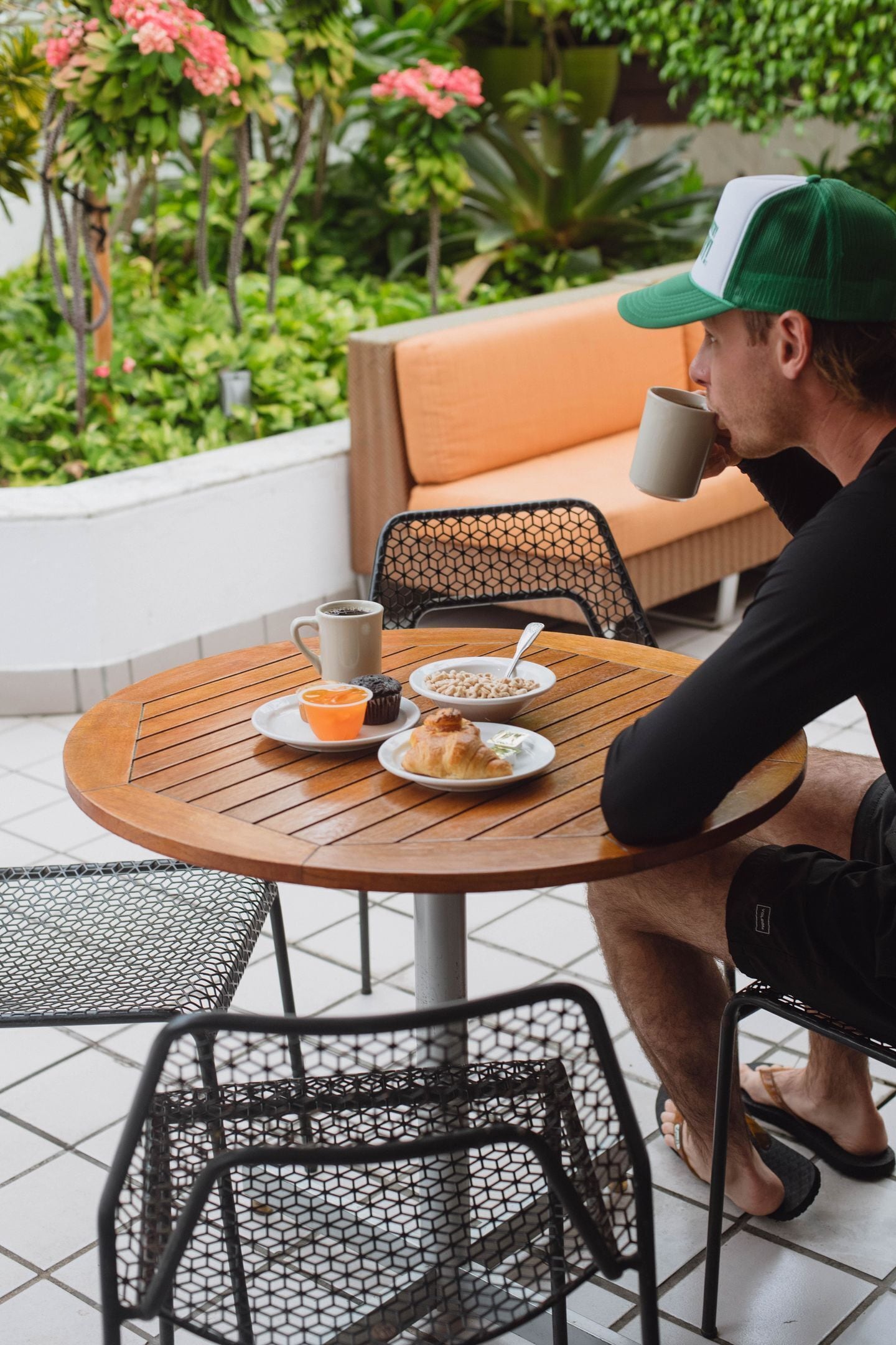 A person seated at an outdoor round table with a cup, a bowl of food, and a muffin on a tray.
