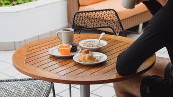 A person seated at an outdoor round table with a cup, a bowl of food, and a muffin on a tray.