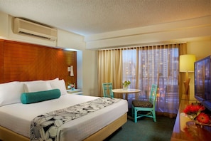 A hotel room with a bed, a TV, a desk with a lamp, a chair, and a window with curtains.