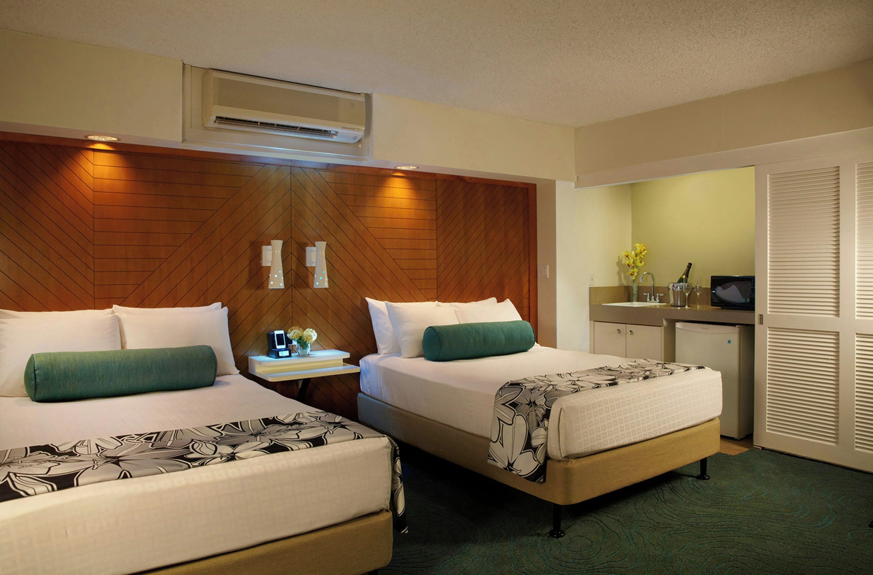A hotel room with two beds, a desk, a minibar, and an air conditioning unit.