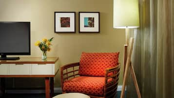 Habitación de hotel con televisión, escritorio, silla, lámpara y dos cuadros en la pared.