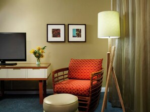 Habitación de hotel con televisión, escritorio, silla, lámpara y dos cuadros en la pared.