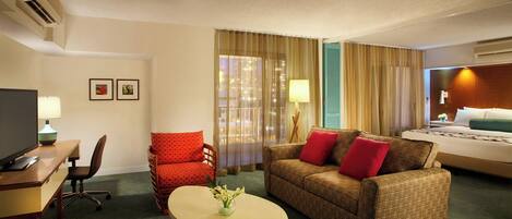 Una habitación de hotel con cama, sofá, escritorio y silla, y televisor.