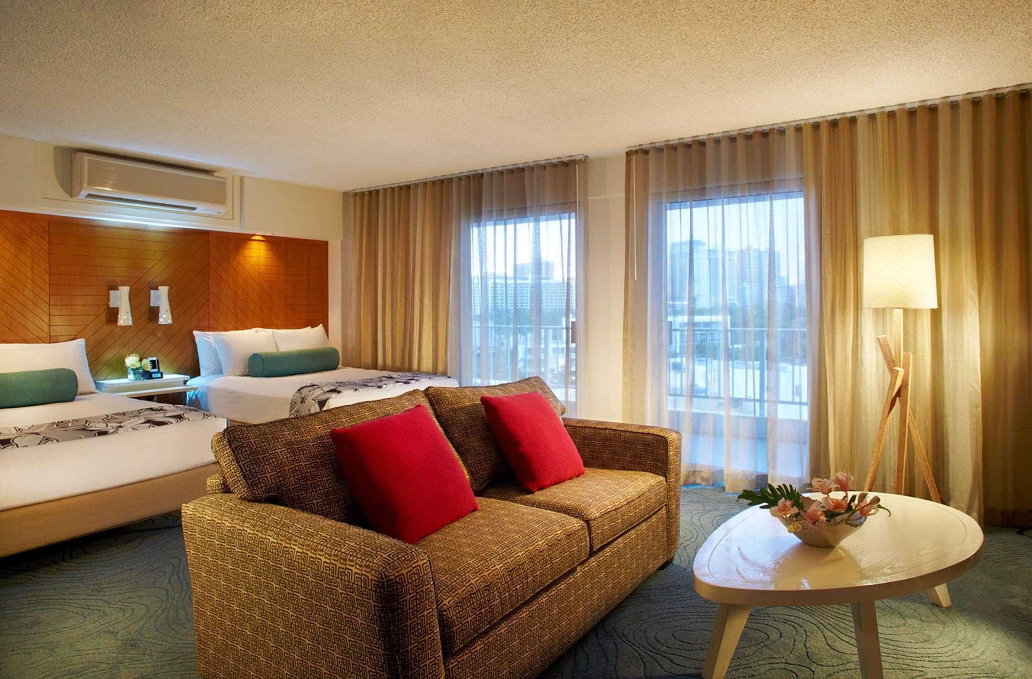 A hotel room with a bed, a sofa, a small table, and a window with curtains.