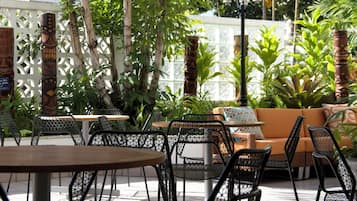 Un área de estar al aire libre con mesas y sillas, rodeada de follaje y detalles decorativos.