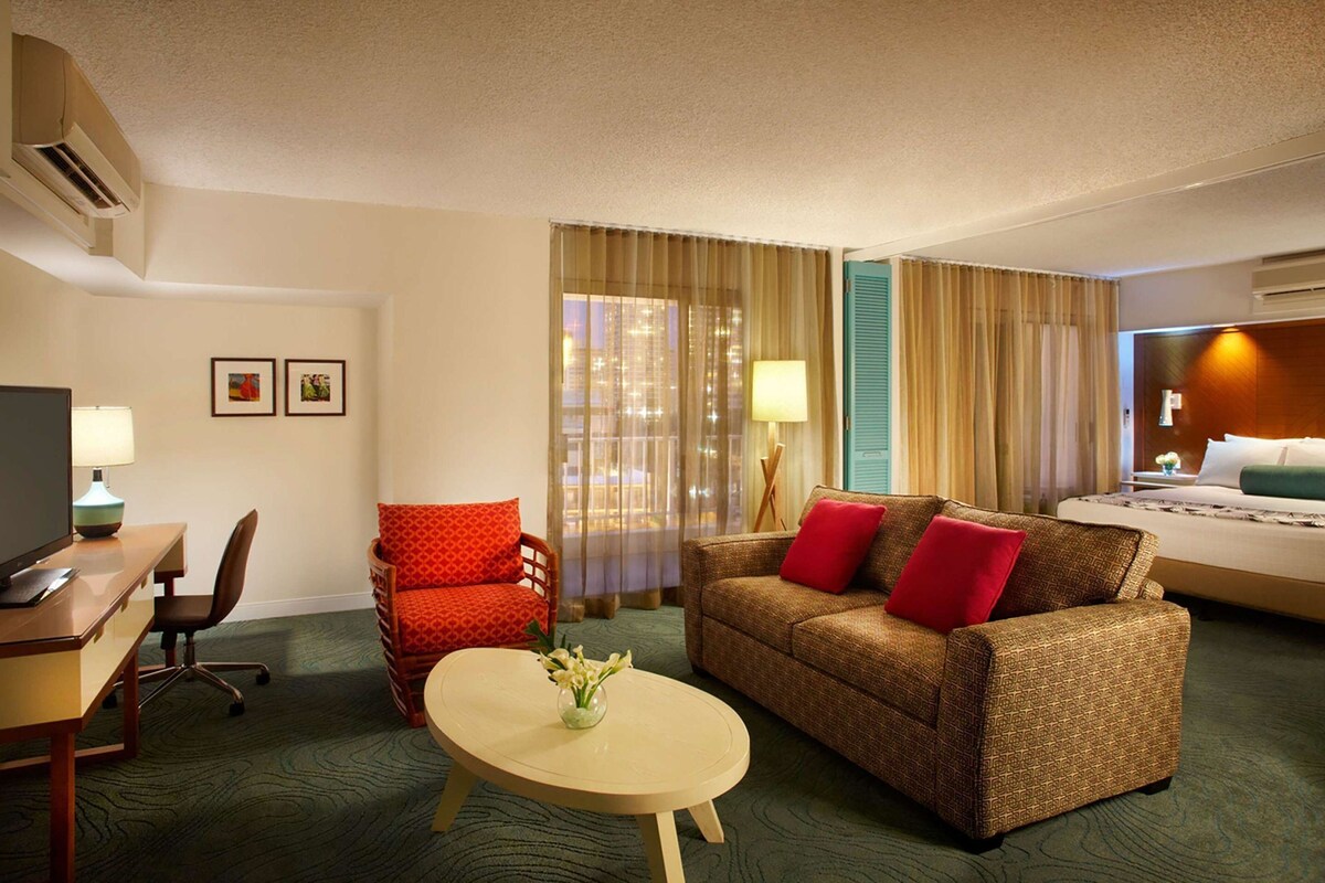 A hotel room with a bed, a sofa, a desk with a computer, a chair, and a lamp.