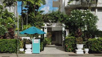 A hotel entrance with a sign, a pathway, and lush greenery.