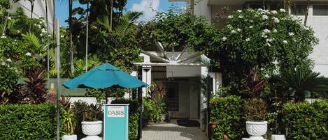 A hotel entrance with a sign, a pathway, and lush greenery.