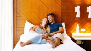 Una pareja en una cama en una habitación con paneles de madera y una mesita de noche con una botella.