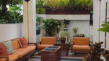 A cozy outdoor seating area with wicker furniture and a variety of potted plants.