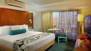 Una habitación de hotel con cama, televisión, escritorio con lámpara, silla y ventana con cortinas.