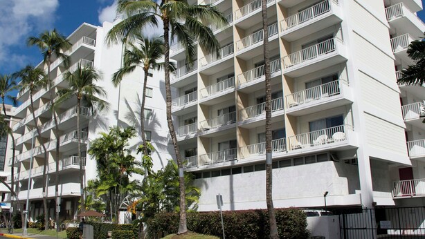 Un hotel de varios pisos con balcones, palmeras y cielo despejado.