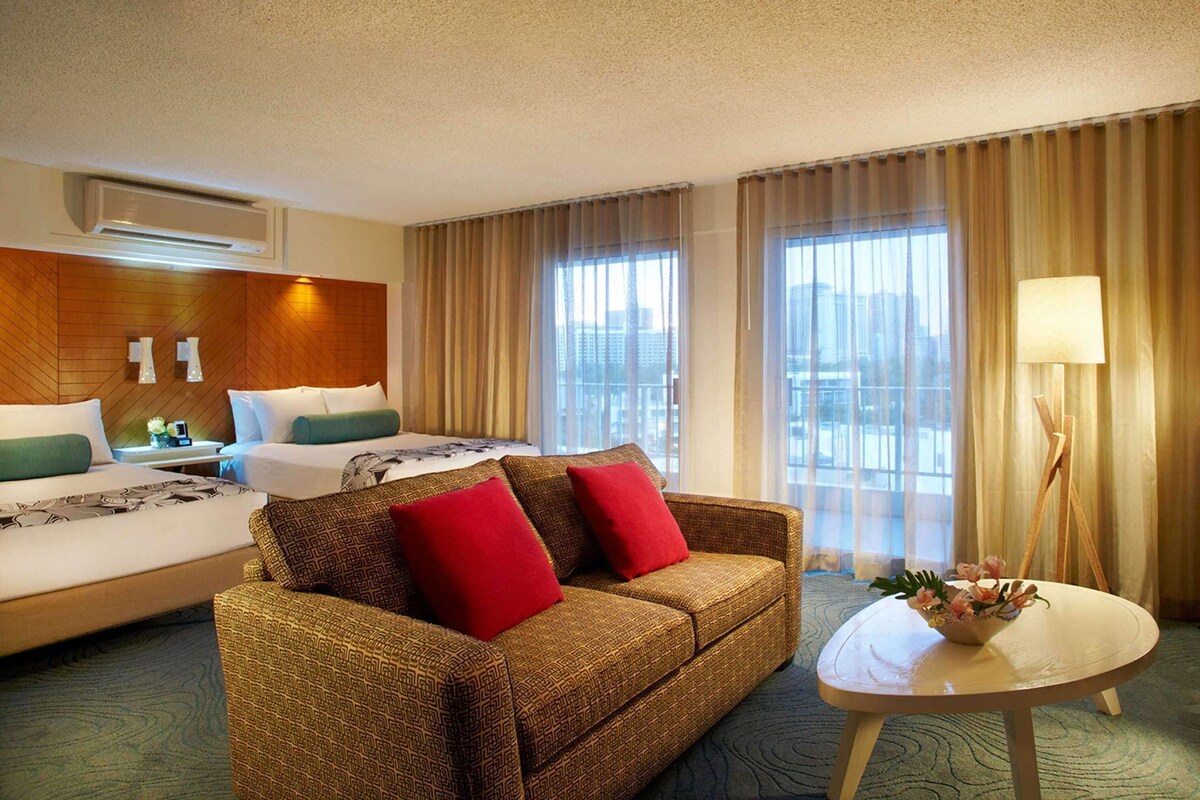A hotel room with a bed, a sofa, a small table, and a window with curtains.