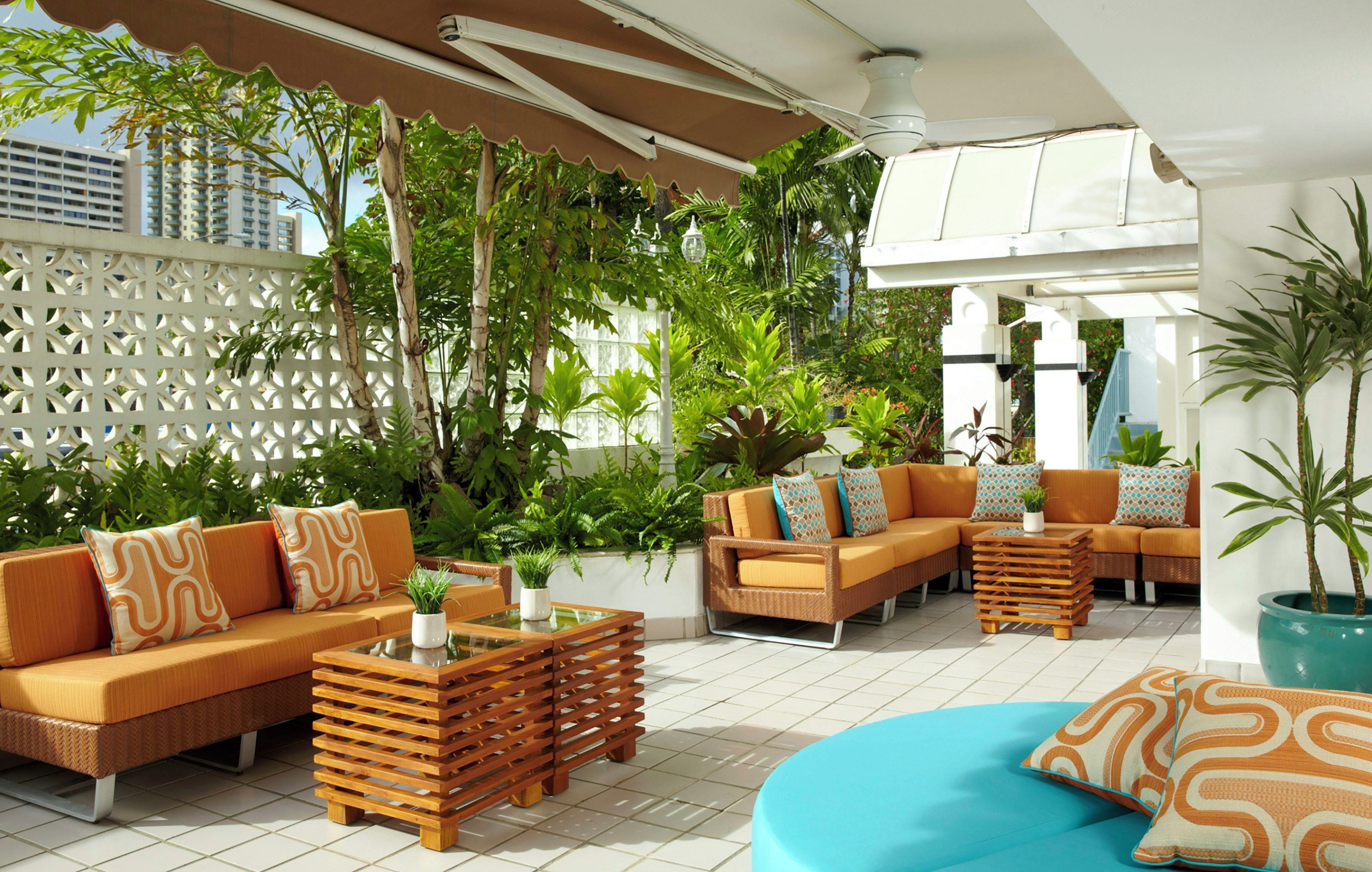An outdoor seating area with sofas and a coffee table, surrounded by lush greenery and a white lattice fence.