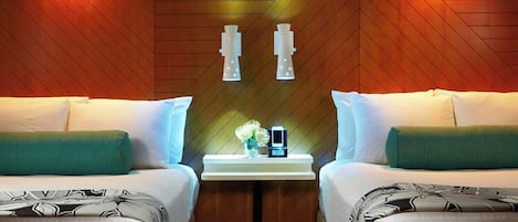 A hotel room with two beds, a nightstand with a clock and a vase of flowers, and wooden paneling on the walls.