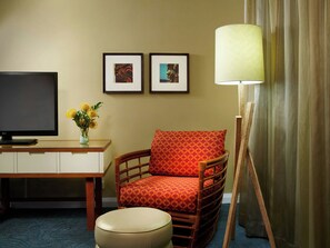 A hotel room with a television, a desk, a chair, a lamp, and two framed pictures on the wall.