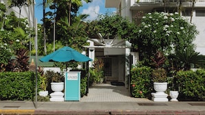 A hotel entrance with a sign, a pathway, and lush greenery.