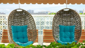 Two hanging chairs with cushions, a white lattice structure, and a view of buildings in the background.