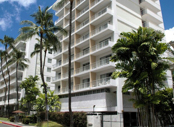A multi-story hotel with balconies, palm trees, and a clear sky.
