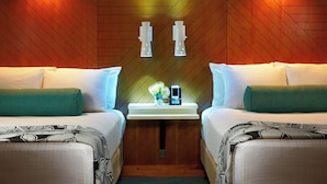 A hotel room with two beds, a nightstand with a clock and a vase of flowers, and wooden paneling on the walls.