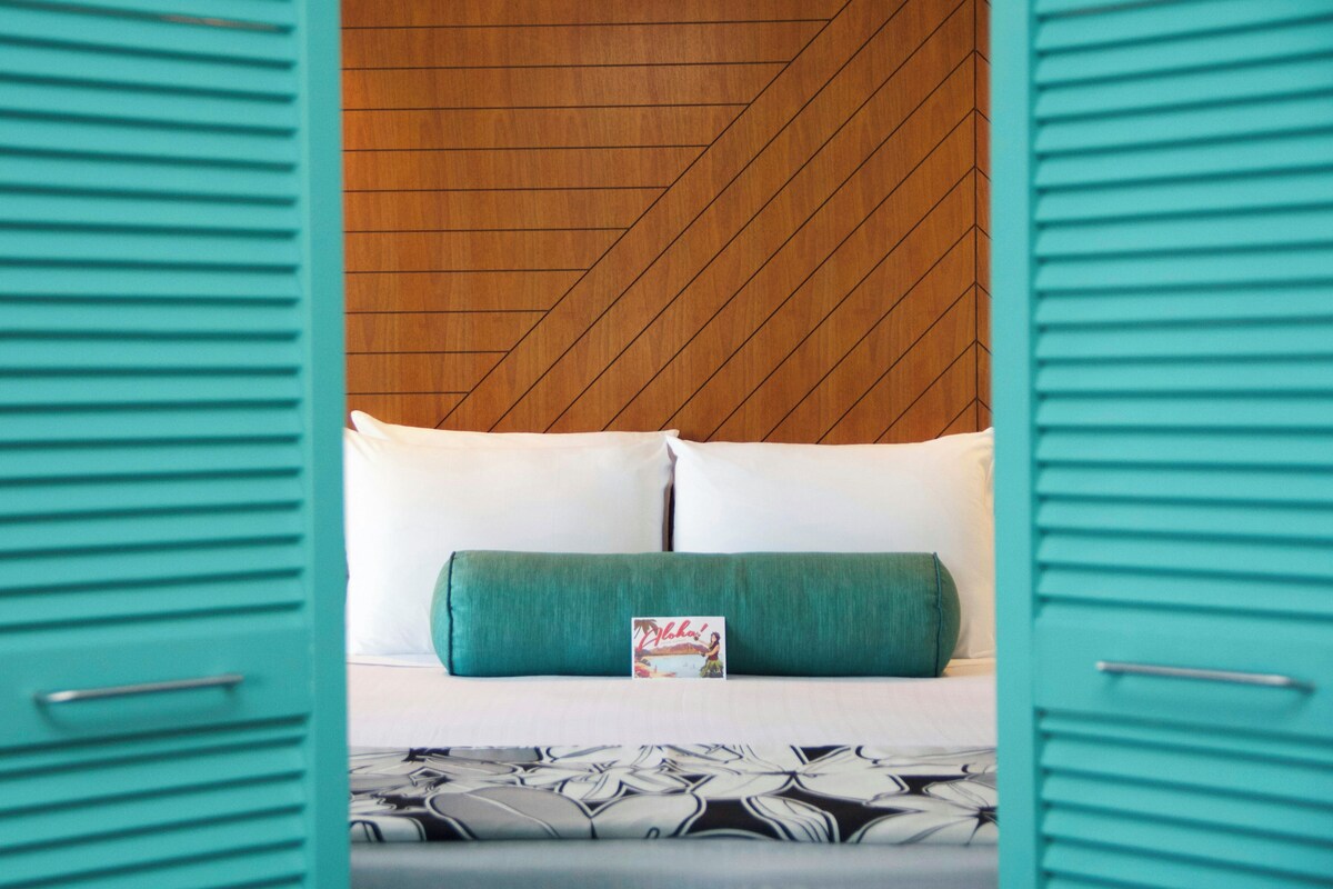 A hotel room with a bed, pillows, and a magazine on the bed.