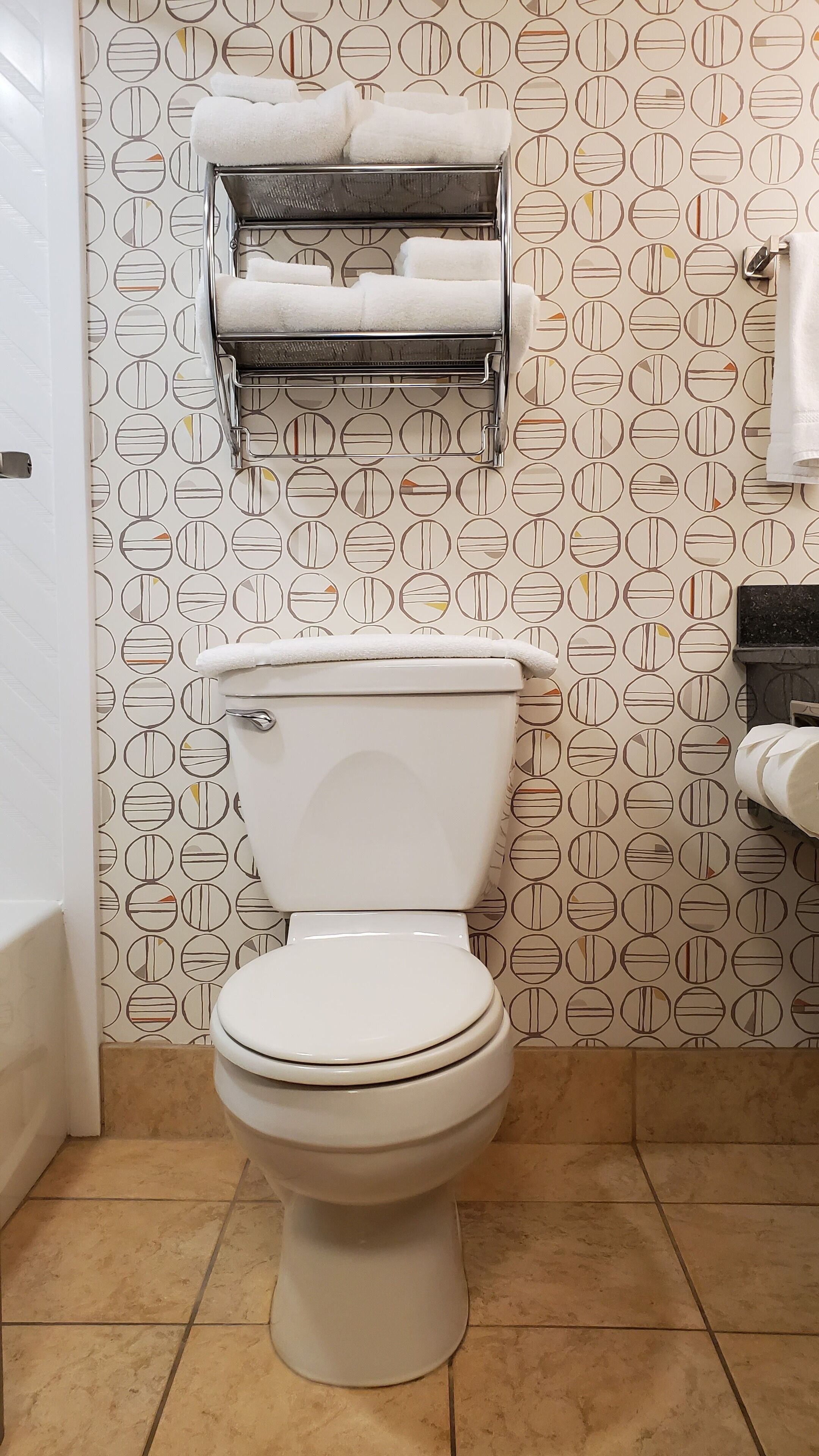 A toilet with a white lid and tank, a towel rack above it, and a patterned wall.