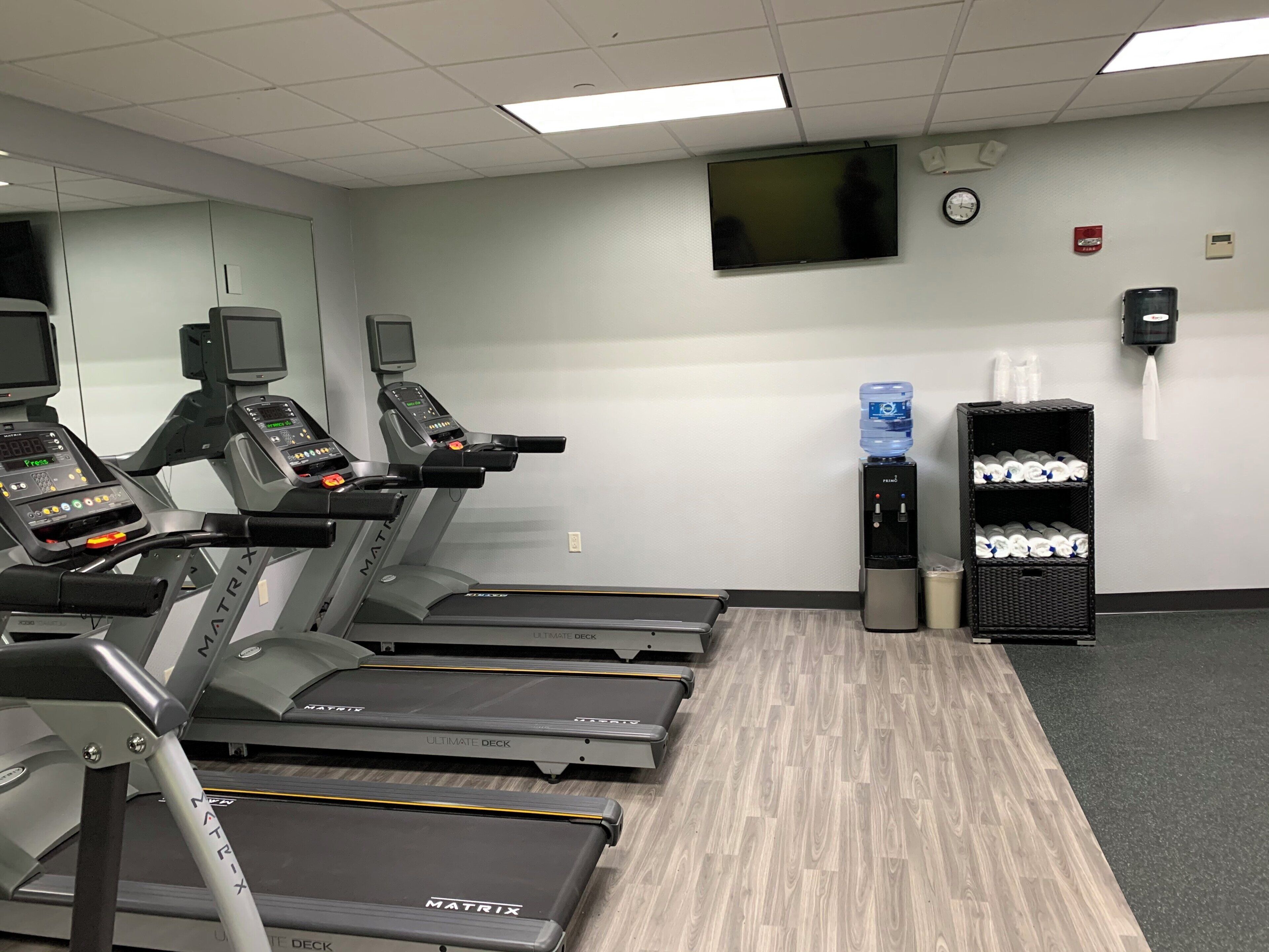 Un gimnasio con cintas de correr, dispensador de agua y un reloj en la pared.