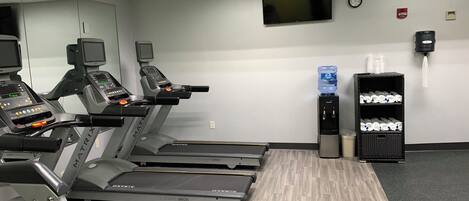 A fitness center with treadmills, a water dispenser, and a clock on the wall.