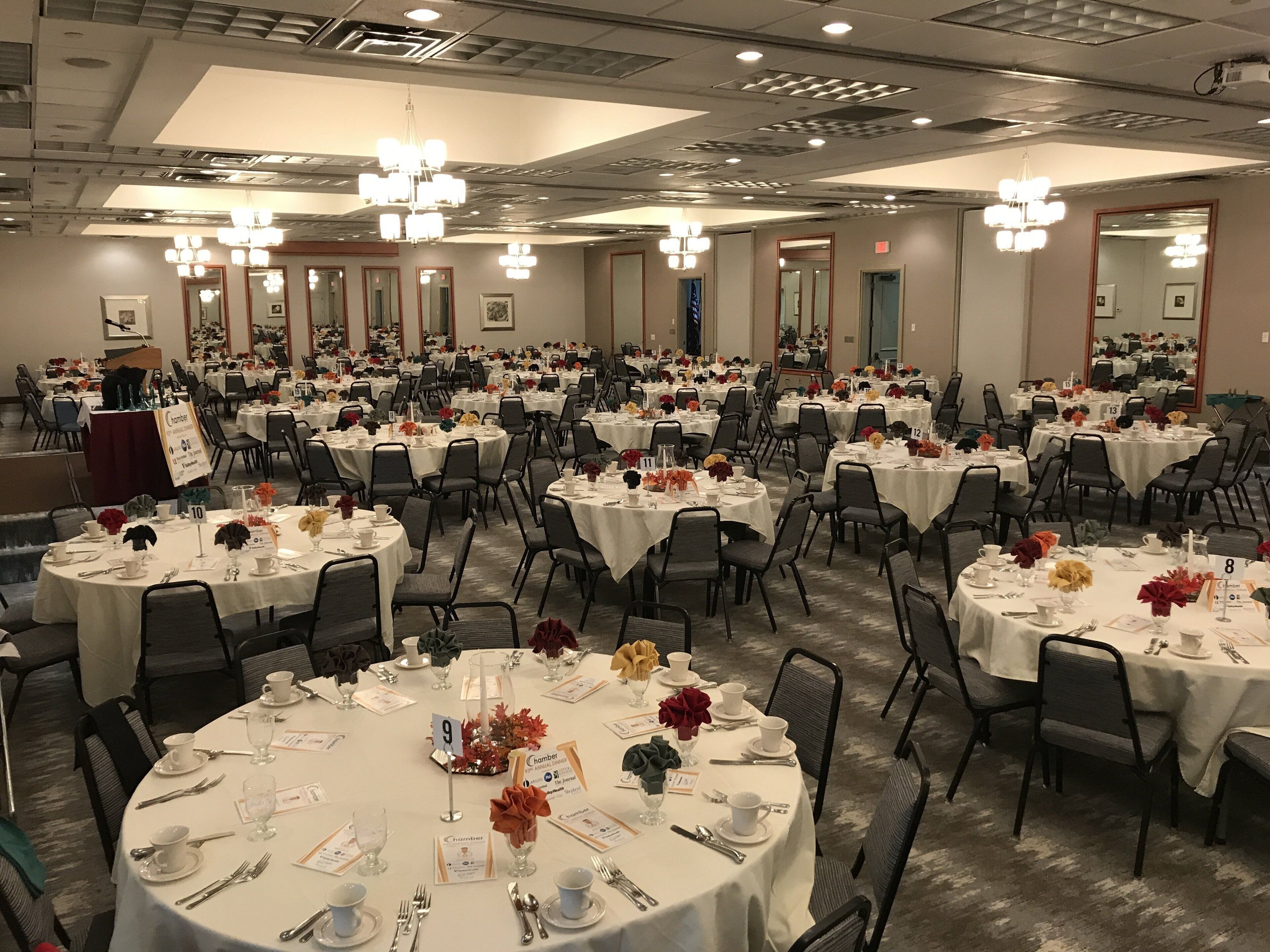 A large banquet hall with round tables, each set with white tablecloths, silverware, and floral centerpieces.