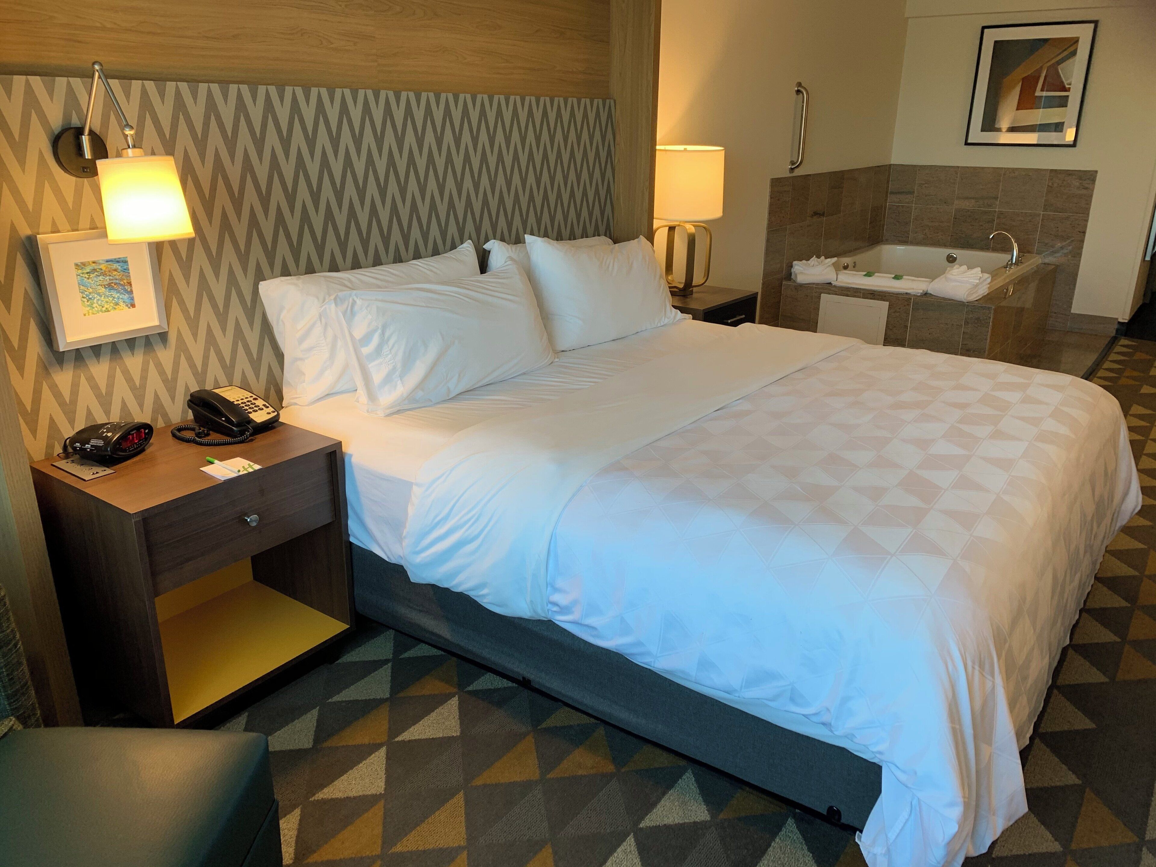 Ein Hotelzimmer mit Bett, Nachttischlampen, Telefon, einem kleinen Tisch und einem Badezimmer mit Badewanne.