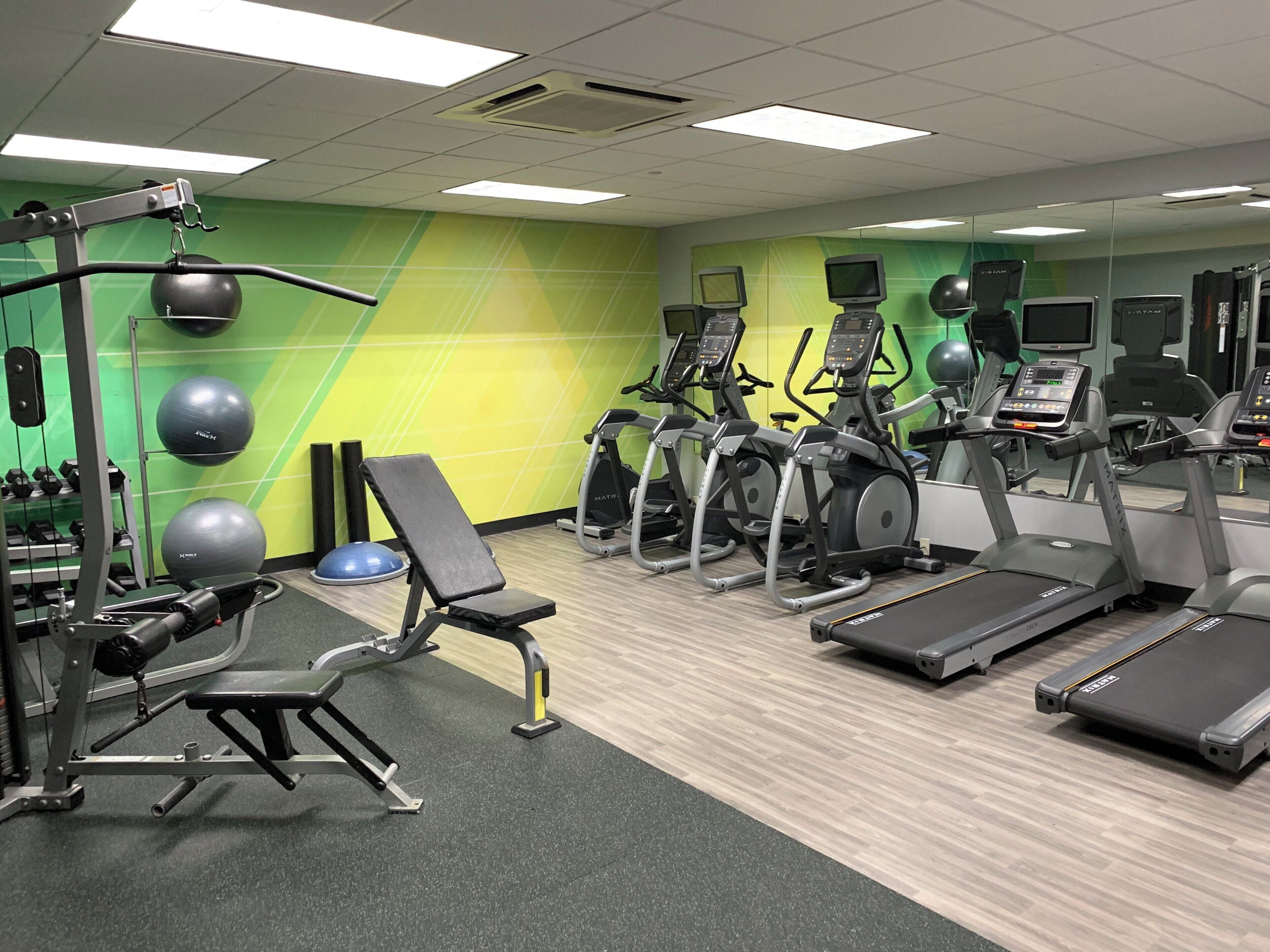 Une salle de sport équipée de matériel d’exercice, de tapis de course et d’un téléviseur fixé au mur.