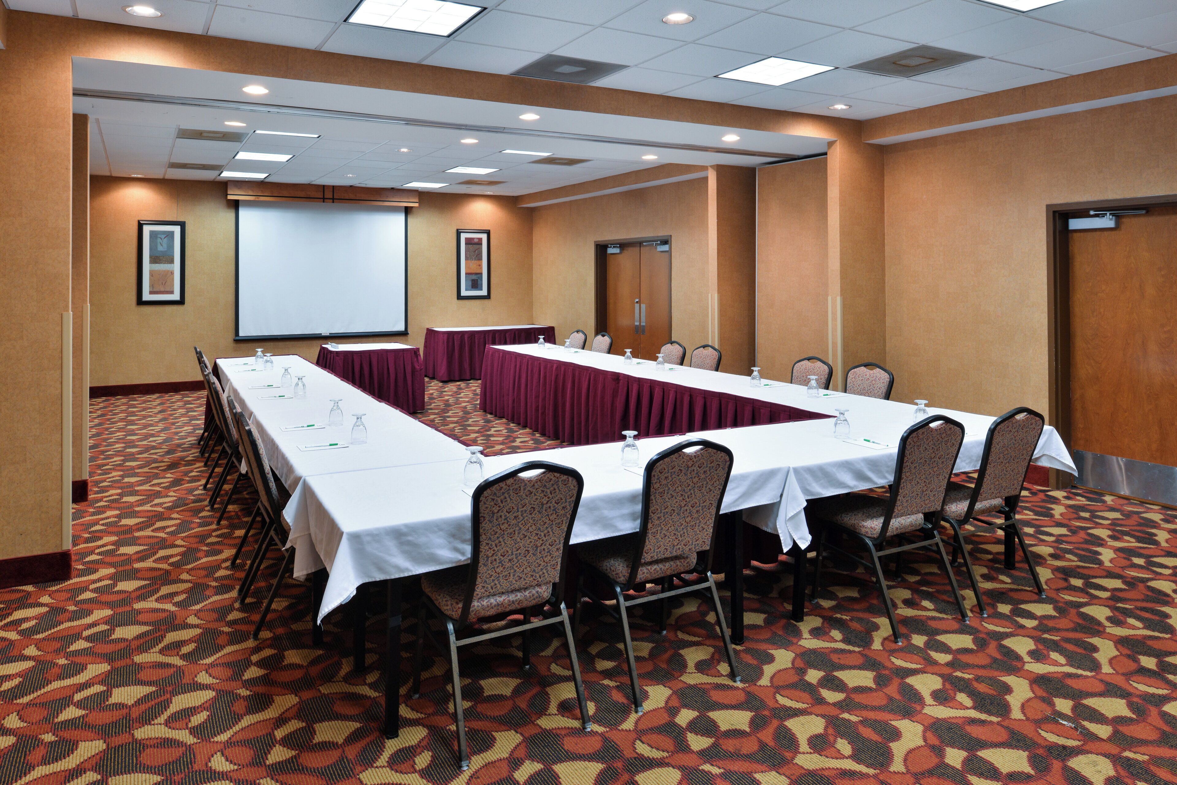 A conference room with a long table, chairs, a projector screen, and a carpeted floor.