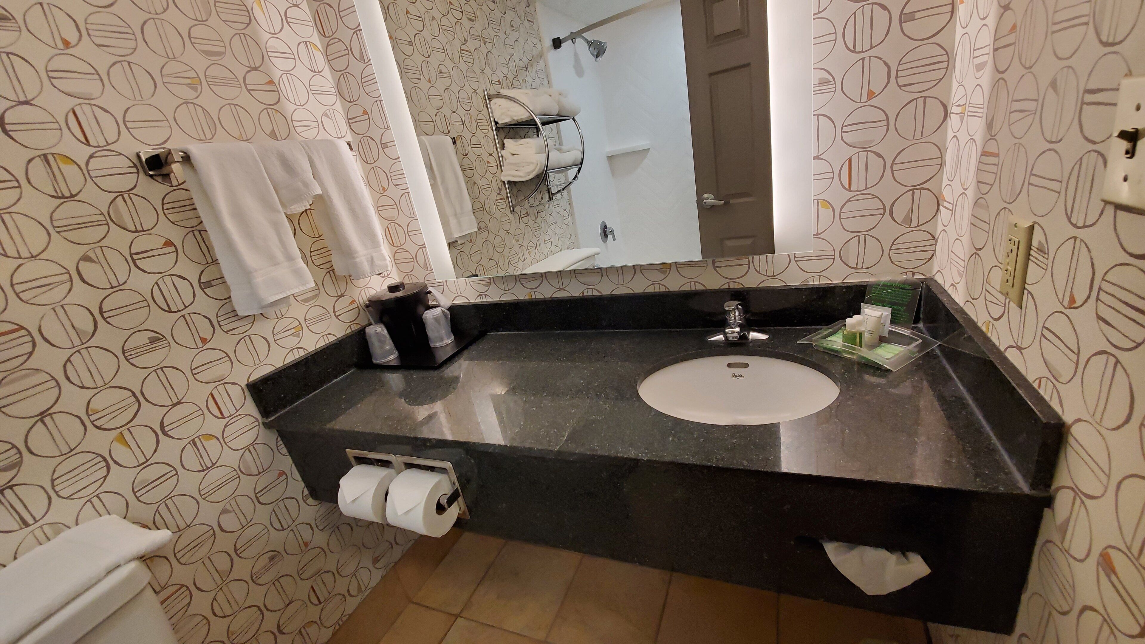 A bathroom with a black countertop, a white sink, a mirror, and a towel rack.