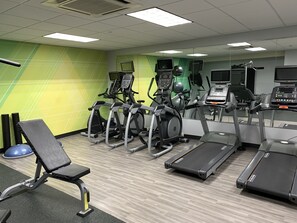 Une salle de sport équipée de tapis de course, de vélos elliptiques et d’un banc de musculation.