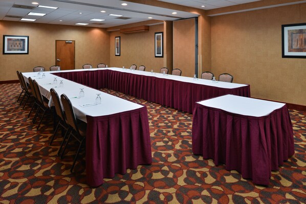 Une salle de conférence avec de longues tables, des chaises et un tapis à motifs.