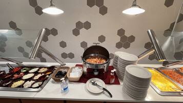 A buffet setup with various food items, a hot pot, and stacked plates.