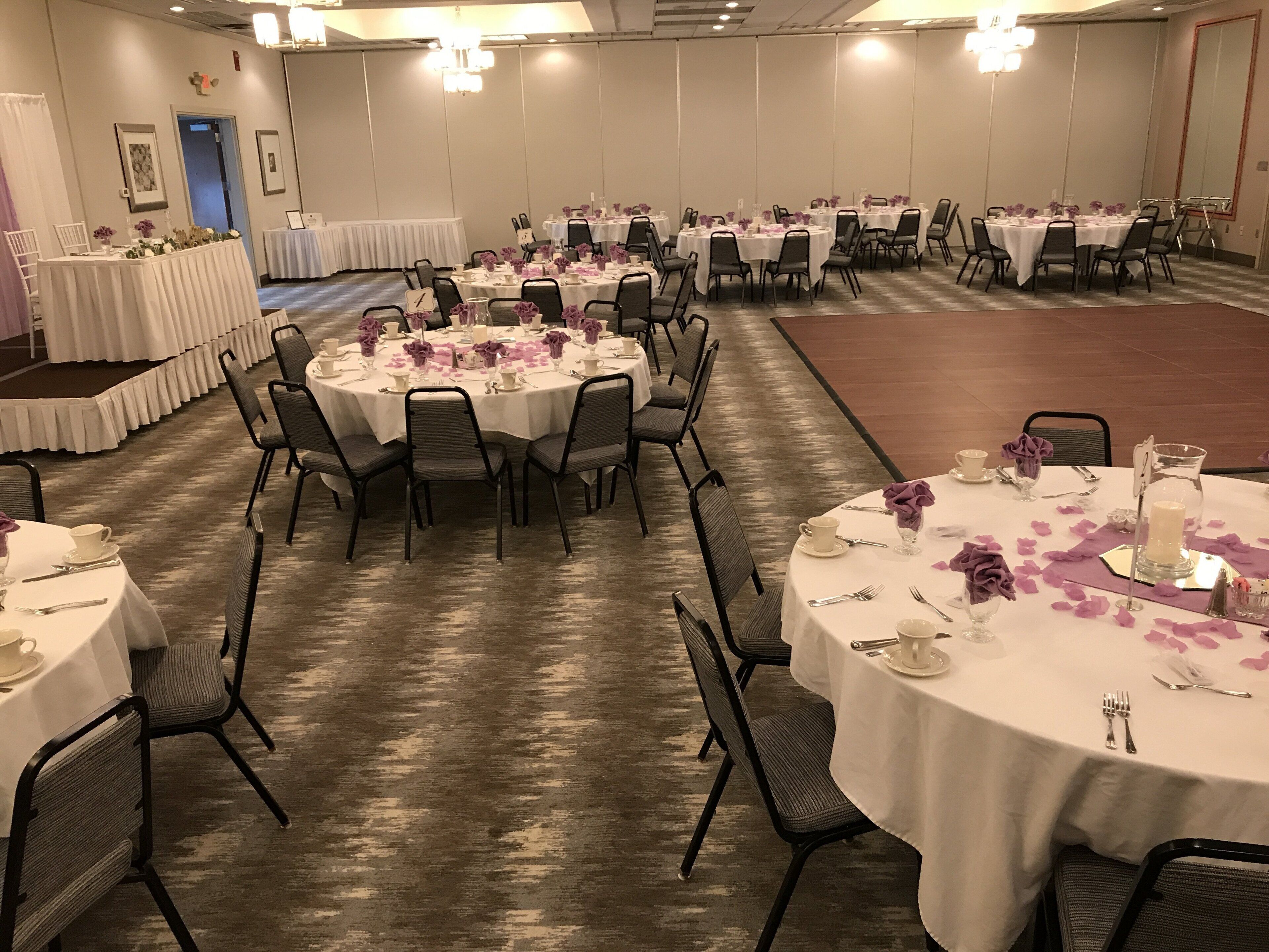 A banquet hall with round tables set for dining, featuring white tablecloths and purple floral centerpieces.