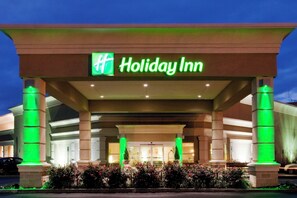 A Holiday Inn hotel entrance with a prominent green sign, columns, and a well-lit facade. - Holiday Inn Martinsburg by IHG (Martinsburg)