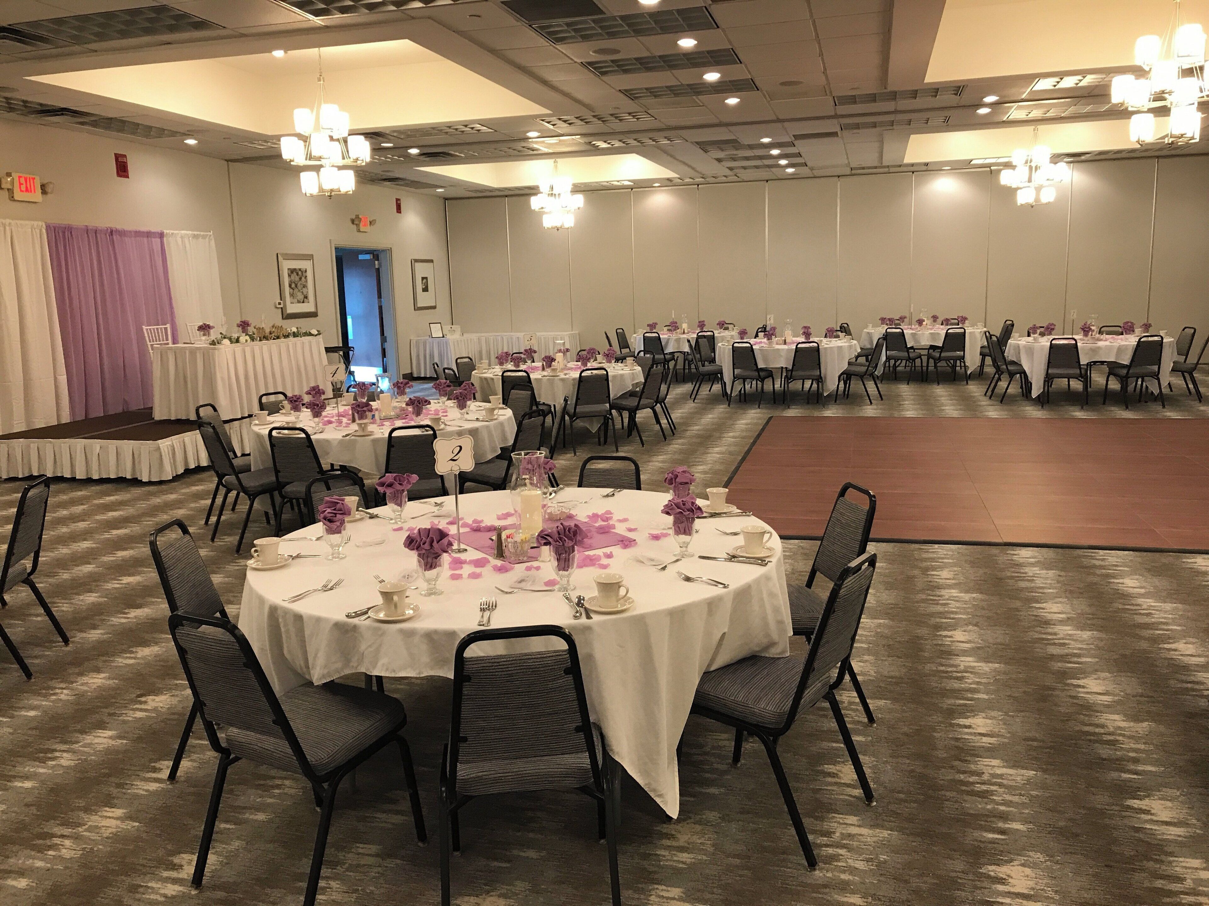 A banquet hall with round tables, chairs, and chandeliers.
