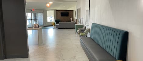 Un vestíbulo moderno con piso de mármol, un sofá verde, un reposapiés amarillo y un televisor montado en la pared.