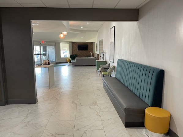 A modern lobby with a marble floor, a green sofa, a yellow ottoman, and a TV mounted on the wall. - Holiday Inn Martinsburg by IHG (Martinsburg)