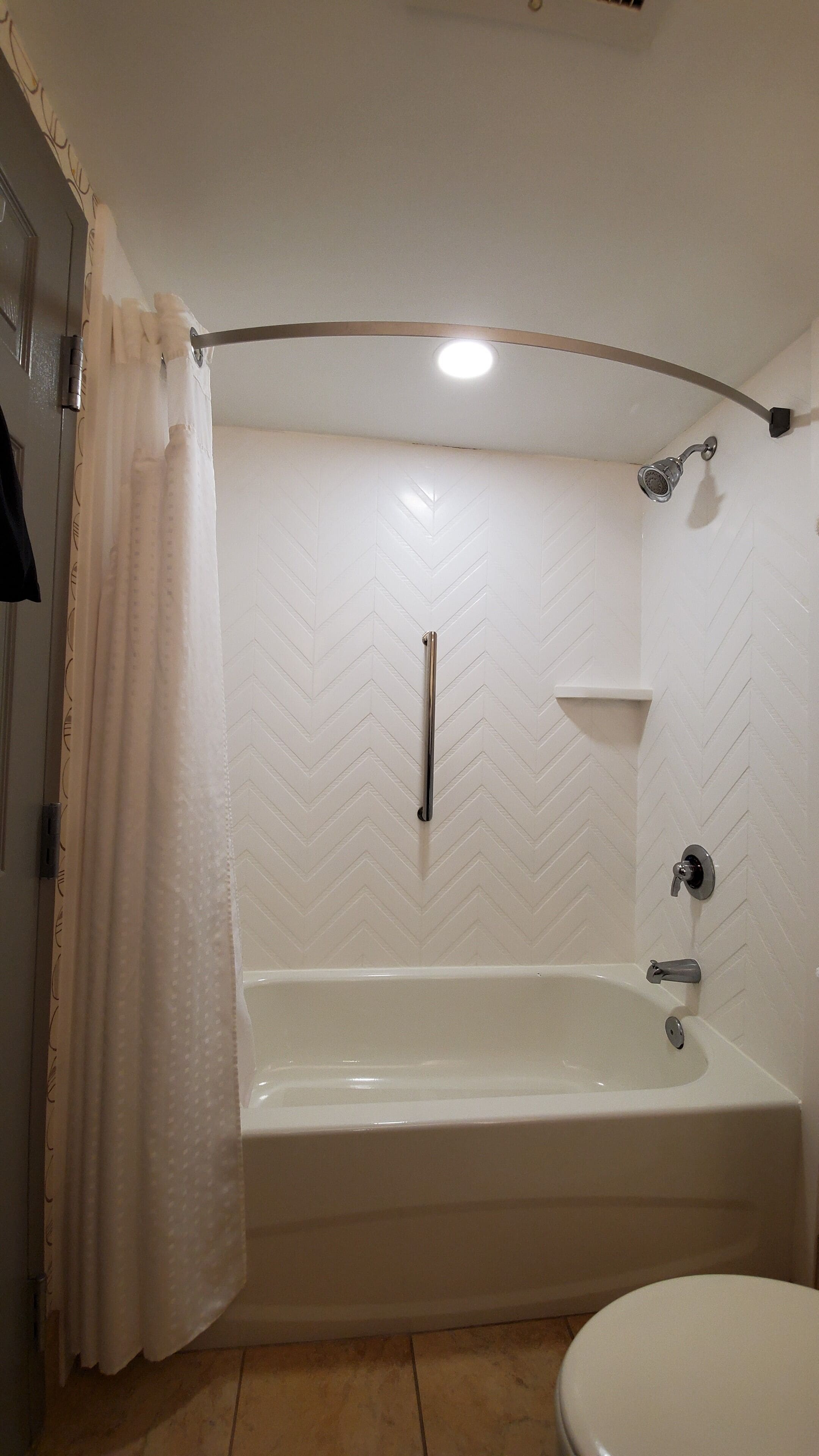 Une salle de bain avec une baignoire blanche, une pomme de douche, des toilettes et un porte-serviettes.