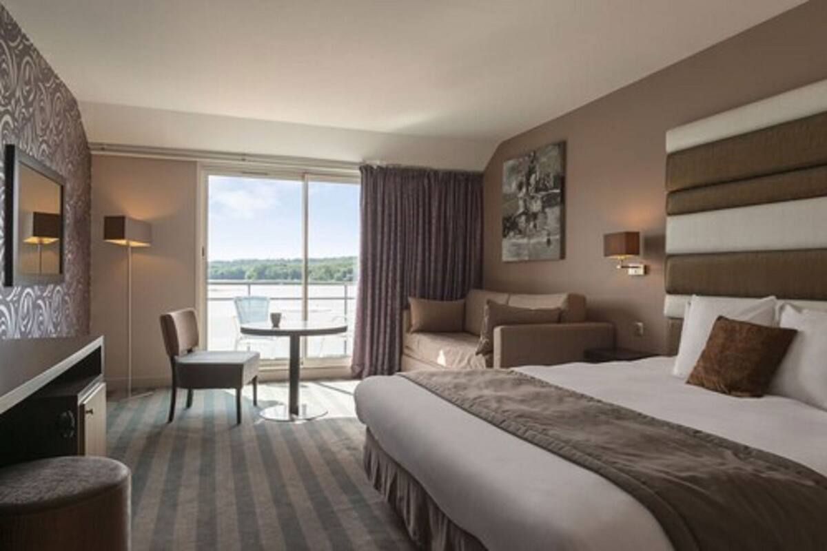 Hotelkamer met een groot bed, een bureau, een stoel en uitzicht op het omliggende landschap.