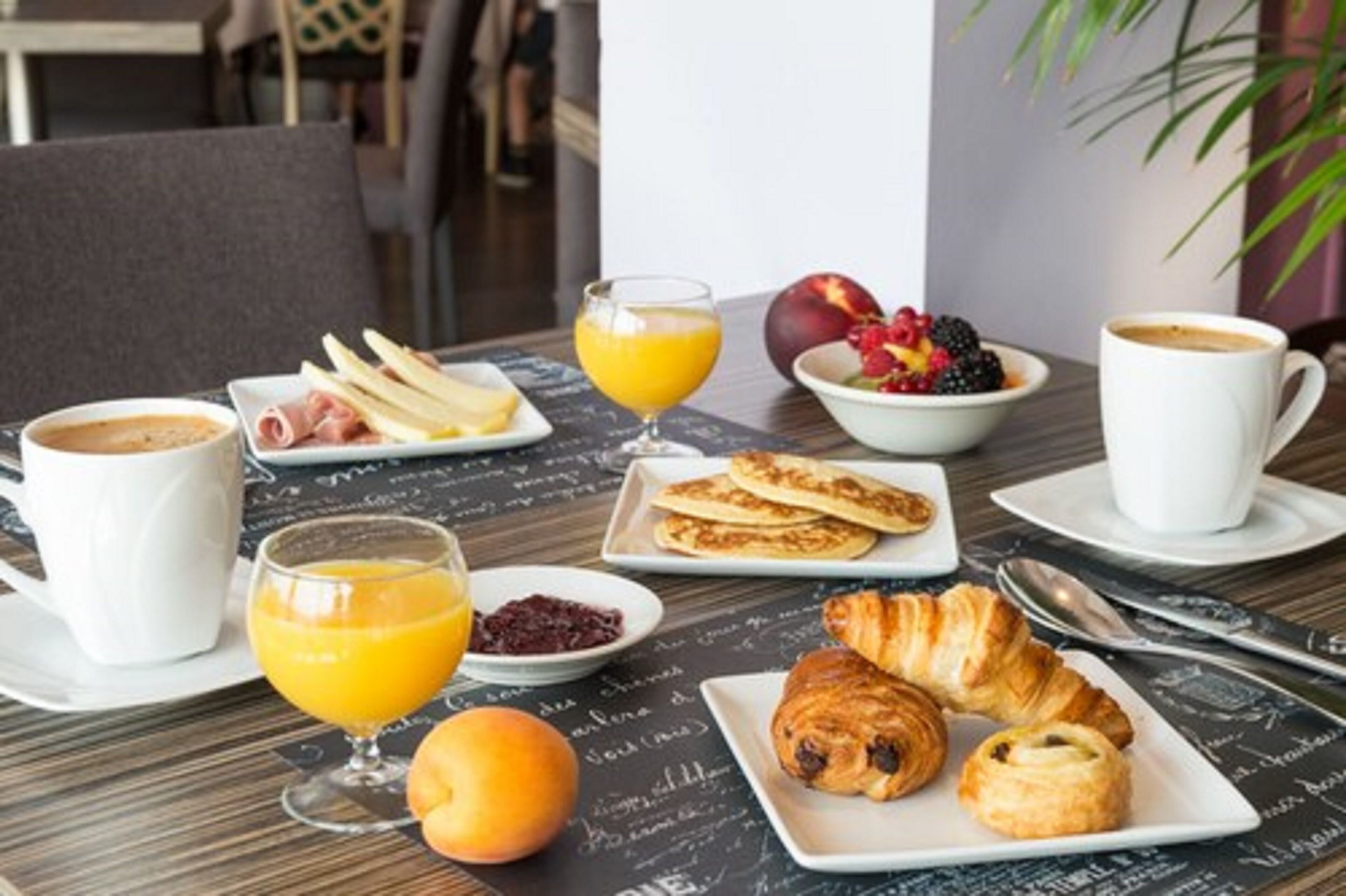 A breakfast setting with croissants, pastries, fruit, and beverages on a table with a chalkboard background.